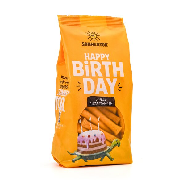 SONNENTOR Happy Birthday Dinkel-Pizzastangen. Gelbe Packung mit Illustration einer Schildkröte, die auf ihrem Rücken eine Torte mit Kerzen trägt. Im Sichtfenster ist das längliche Knabbergebäck zu sehen.
